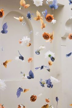 an arrangement of flowers and leaves are suspended from the ceiling in front of a white wall