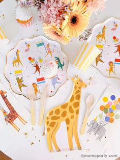 a table topped with plates and cupcakes covered in giraffe paper decorations