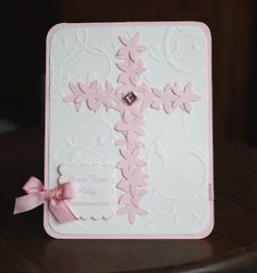 a pink and white card with a cross on the front that has a ribbon around it