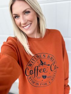 a woman with blonde hair wearing an orange sweatshirt and smiling at the camera while standing in front of a white wall