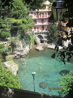 people are swimming in the clear blue water near a pink building and some green trees