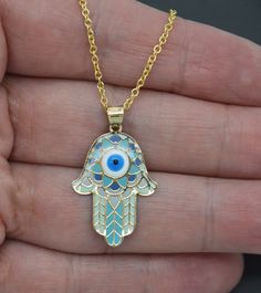 "Beautifully crafted in solid 14K yellow gold, this gorgeous 14k Yellow Gold Ocean Blue Enamel Hamsa Evil Eye Pendant + 18\" Chain is adorned with vibrant blue enamel. It is beautifully paired with an 18-inch chain, making it a perfect addition to any jewelry collection. Unique and eye-catching, its stylish design will perfectly complement any look. Add a touch of luxury with this piece and enjoy its unique symbolism and stunning beauty!  Specifications: Metal: Real 14K Yellow Gold (Stamped, 14K Spiritual Blue Pendant Jewelry, Handmade Spiritual Enamel Necklaces, Blue Spiritual Pendant Necklace, Spiritual Gold Enamel Necklace, Blue Metal Necklace With Evil Eye, Chain Fashion, Gold Chain With Pendant, Evil Eye Pendant, Evil Eye