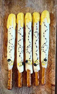 four yellow and white candles are lined up on a wooden surface, with black designs