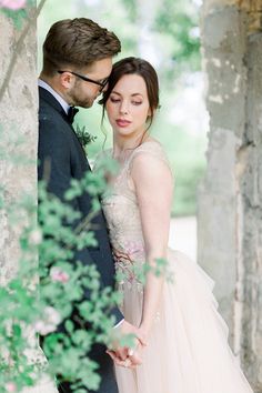 a man and woman standing next to each other in front of a stone wall with greenery