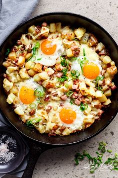 an iron skillet with eggs and potatoes in it on a gray surface next to a spoon