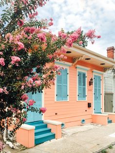 a house with blue shutters and pink flowers on the front door is next to a tree