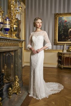 a woman standing in front of a fire place wearing a white dress with sheer sleeves