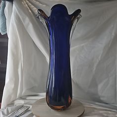 a blue glass vase sitting on top of a wooden stand next to a white sheet