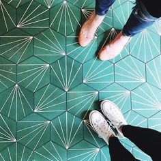 two people standing in front of a green floor with white geometric designs on the ground