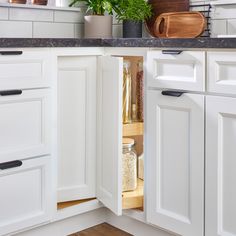 an open cabinet in a kitchen with white cabinets and wood cutting boards on the counter