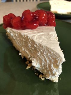 a piece of cheesecake with whipped cream and cherries on top is sitting on a green plate