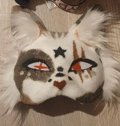 a white and brown cat mask with stars on it's face next to a pair of shoes