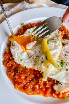 a person is holding a fork and knife over some food on a white plate with red sauce