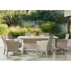 an outdoor dining table with chairs and fire pit in front of plants on the patio