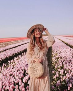 a woman standing in a field full of pink tulips wearing a straw hat