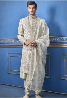 a man standing in front of a blue wall wearing a white suit and shawl