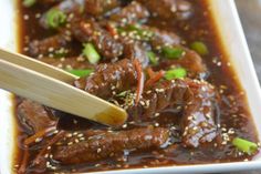 a white plate topped with meat covered in sauce and chopsticks next to it