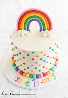 a birthday cake decorated with rainbows and sprinkles on a white tablecloth