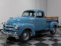 an old blue truck is parked in a room with black and white checkered flooring