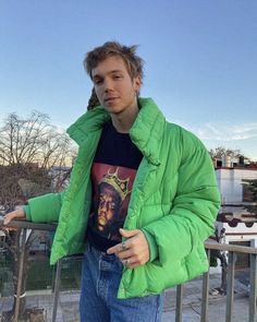 a man in a green jacket is standing on a balcony with his hand on the railing