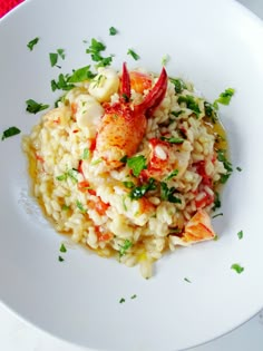 a white plate topped with riso and rice covered in lobsters, garnished with parsley