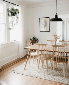 a dining room table and chairs in front of a window with potted plants on it