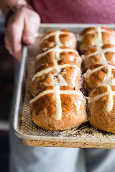 freshly baked hot cross buns with white icing on a baking sheet being held by a person