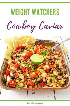 a casserole dish filled with beans, corn and avocado next to tortilla chips