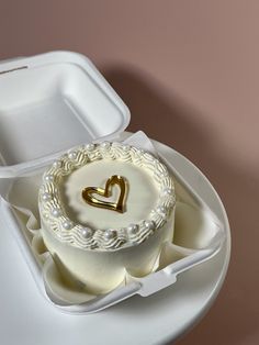 a heart shaped cake in a white box on a table with a pink wall behind it