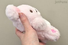 a hand holding a pink stuffed animal with a heart on it's chest and nose