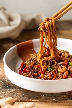 chopsticks holding noodles in a white bowl on a wooden table with other food items