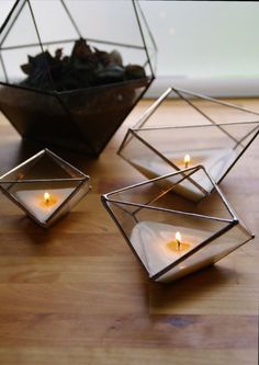 three candles are lit in glass cubes on a wooden table next to a potted plant