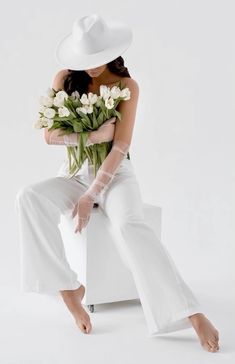 a woman sitting on top of a white chair with flowers in her lap and wearing a white hat