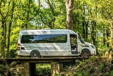 a white van is driving over a bridge in the woods