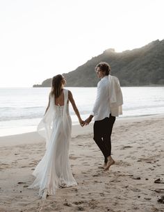 a bride and groom holding hands on the beach