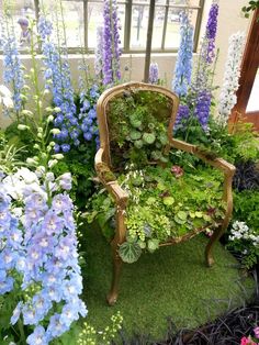 a chair sitting in the middle of a garden filled with purple and white flowers on top of green grass