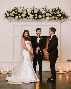 a bride and groom standing next to each other in front of a fireplace with candles