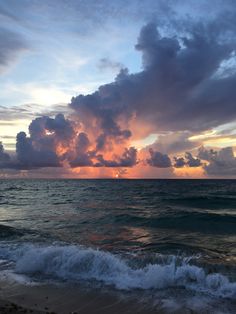 the sun is setting over the ocean with clouds in the sky and waves on the beach