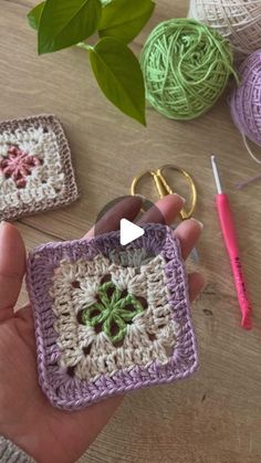 someone is holding a crocheted square keychain in front of some balls of yarn