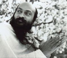 a man with long hair and beard standing in front of trees holding his hands out