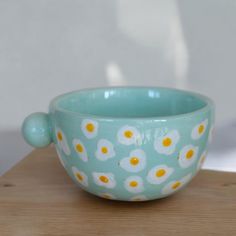 a blue bowl with yellow and white flowers on it sitting on a wooden table next to a wall