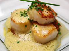 three scallops are on top of some sauce in a square glass dish with green garnish