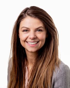 a woman with long brown hair smiling at the camera and wearing a gray blazer