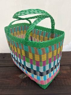 a colorful basket sitting on top of a wooden table next to a white wall with a green handle