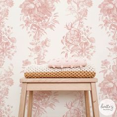 a wooden stool sitting next to a wall with pink flowers on it and a knitted blanket