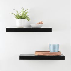 two black floating shelves with plants and bowls on them, one has a blue glass