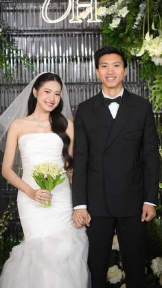 a man and woman standing next to each other in front of a wall with flowers