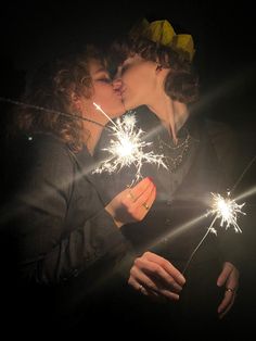 two people kissing while holding sparklers in their hands and wearing hats on top of them