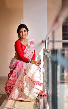 a woman in a red and white sari sitting on the ground with her arms crossed