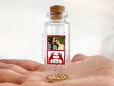 a hand holding a glass bottle with a photo inside and a corked cap on top